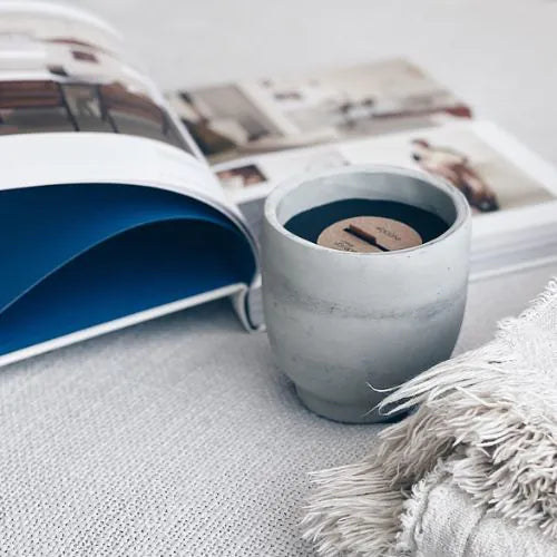 bougie d'intérieure grise avec sa cire noire à côté d'un magazine ouvert