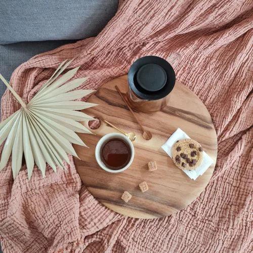 petite planche ronde en bois sur un plaid avec un cookie, du miel et un chocolat