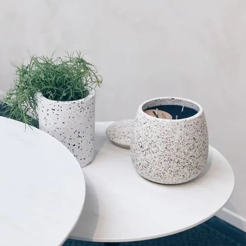 bougie d'intérieure blanche en céramique ouverte sur une petite table et avec une plante à côté