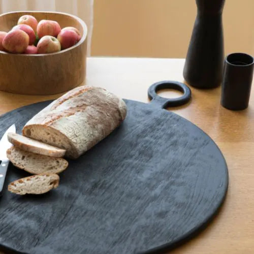 grande planche à découper ronde noire avec du pain coupé dessus sur un table